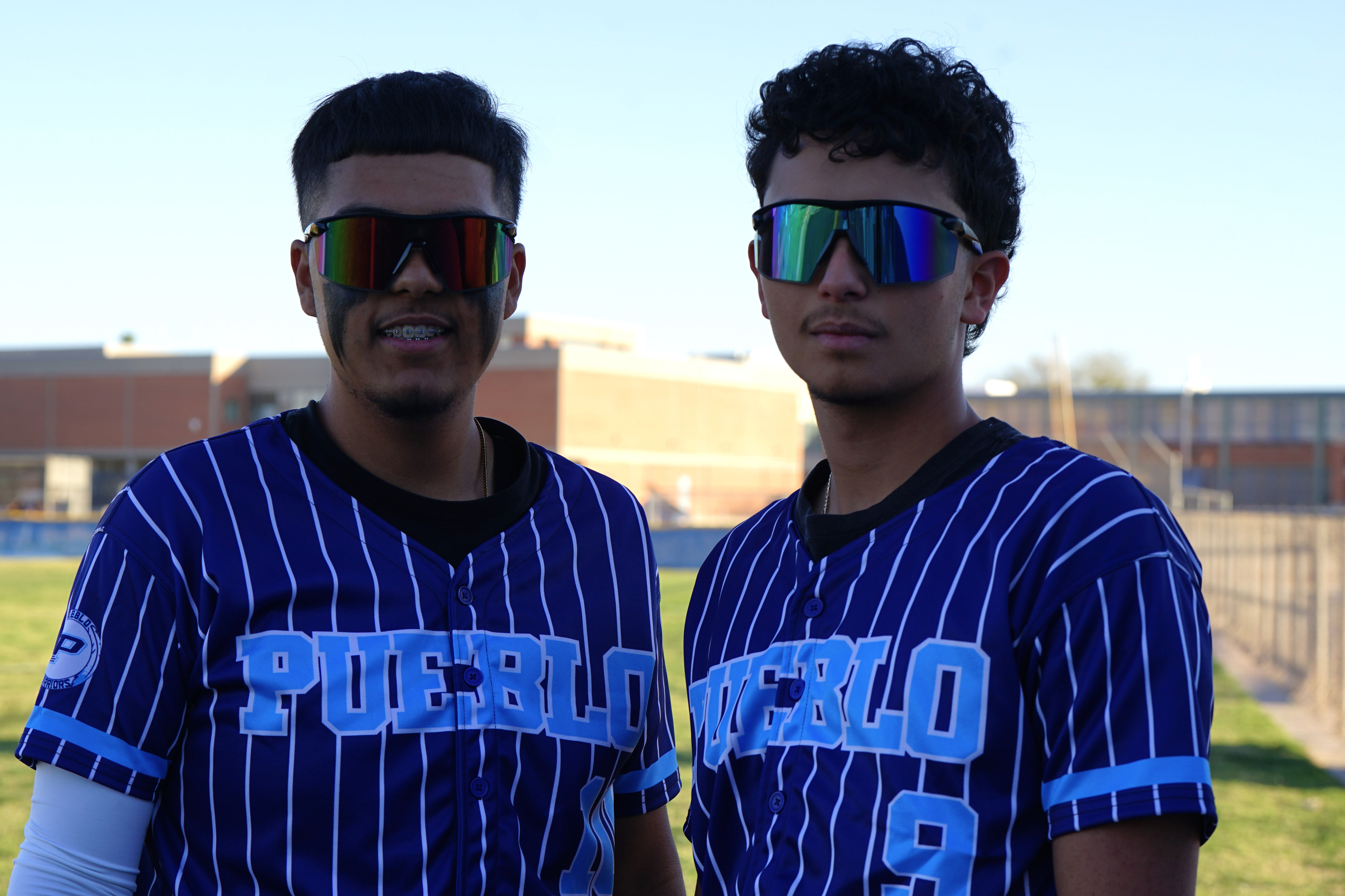 Two Pueblo baseball players smile in their uniforms and sunglasses