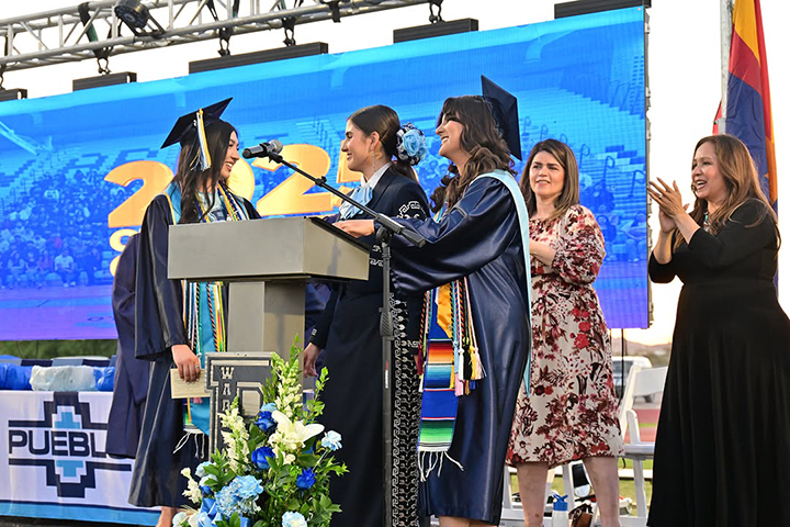 Three graduates laugh together on stage