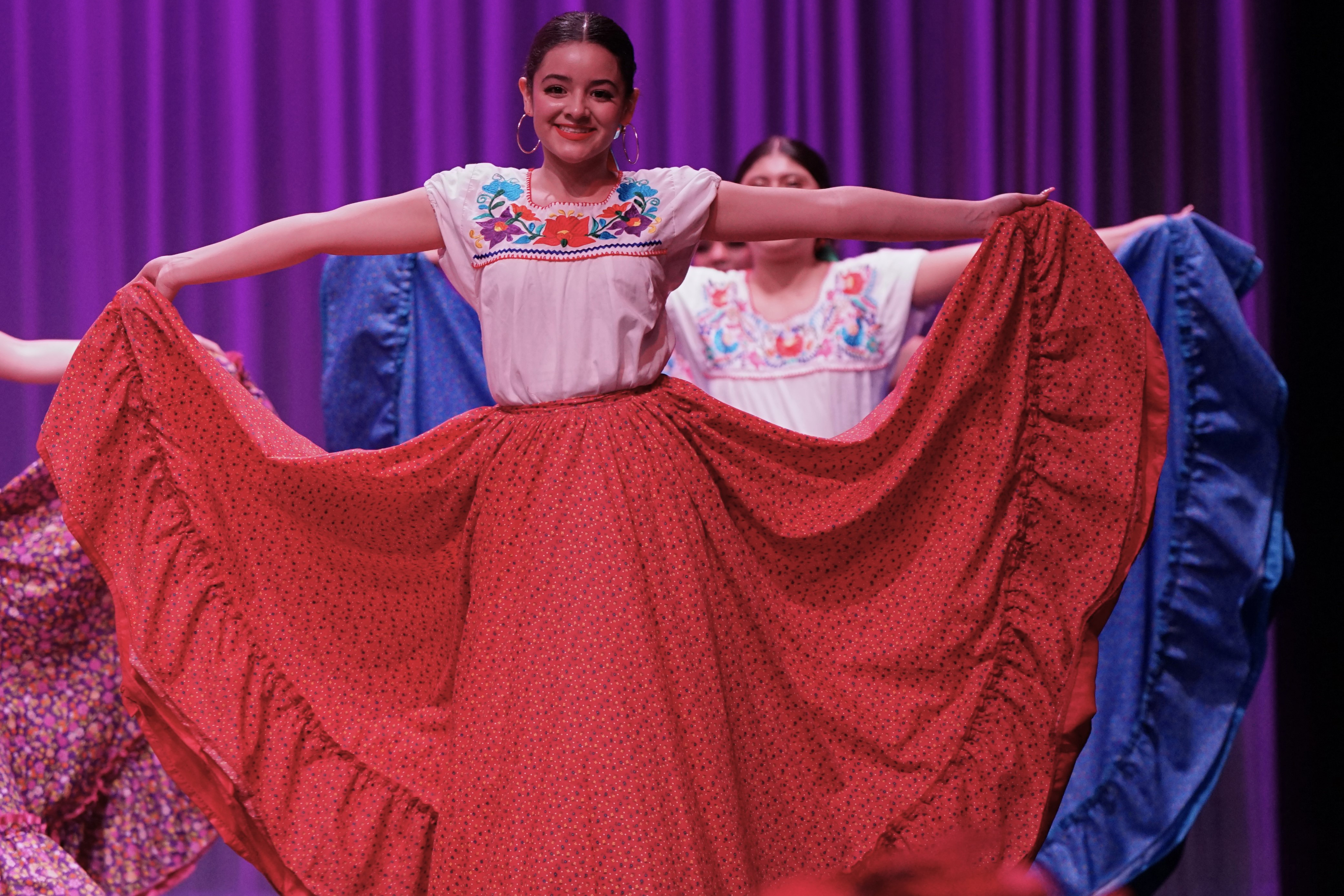 A girl smiles as she dances in her red folklorico dress