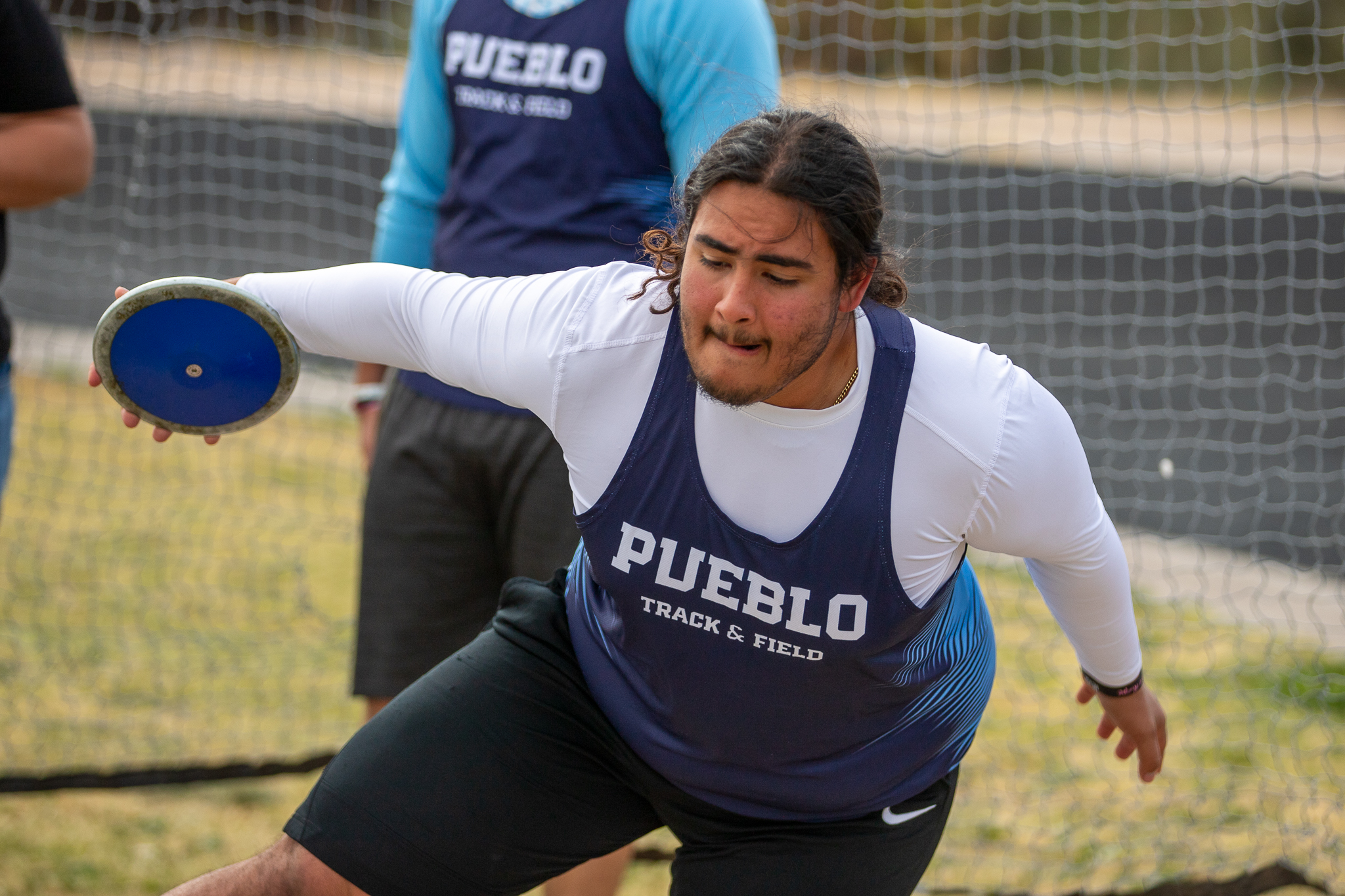 A teen boy squats down to throw a discus