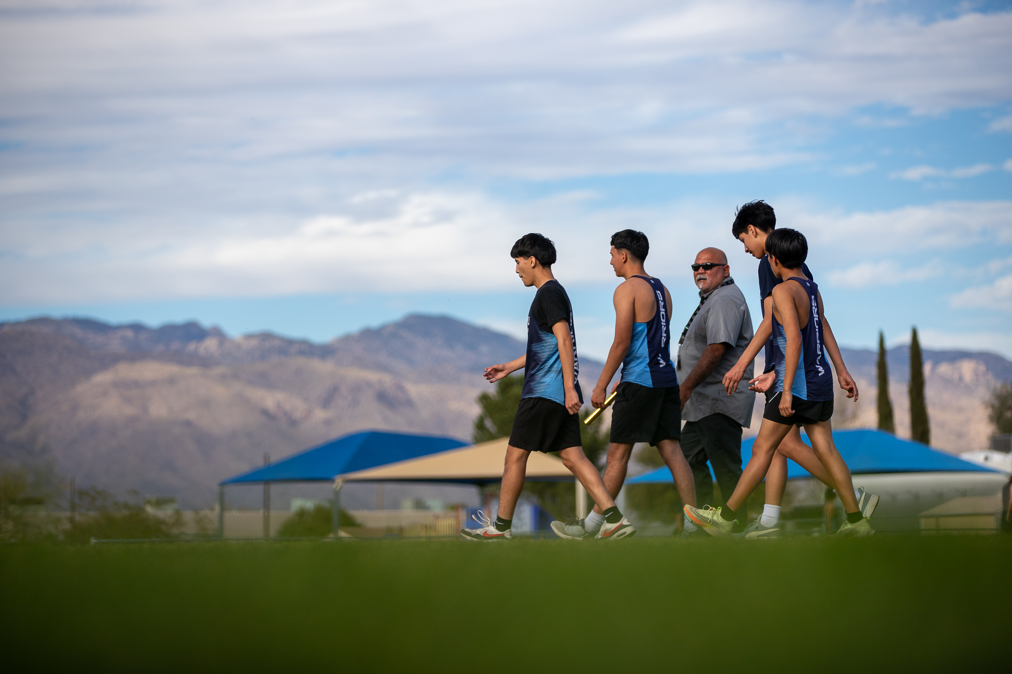 A group of boys from the Pueblo track team walk across the field with a coach