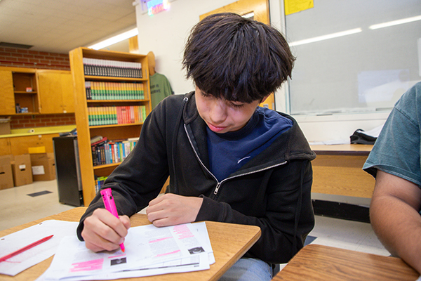 A teen boy uses a pink highlighter to work on his assignment