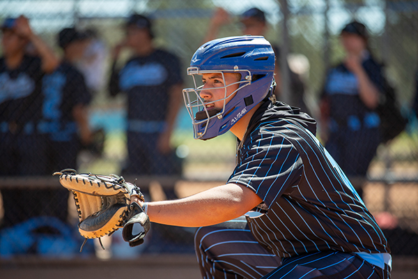The catcher squats over the plate, ready to catch the ball