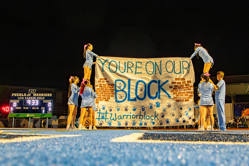Cheerleaders form pyramids next to a banner reading You're on our Block