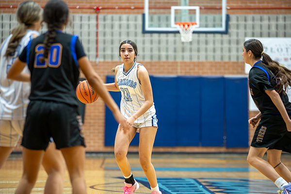 A Pueblo girl looks past her opponents to see where to maneuver with the basketball