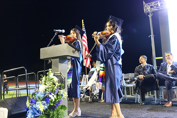 Two teen girl graduates play their violins on stage during the ceremony