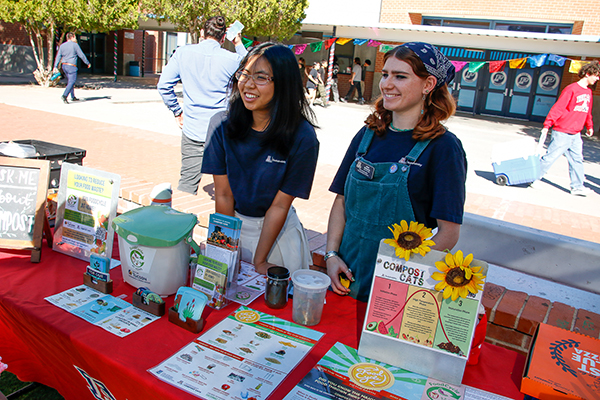 Two teen girls smile behind a table with info about composting