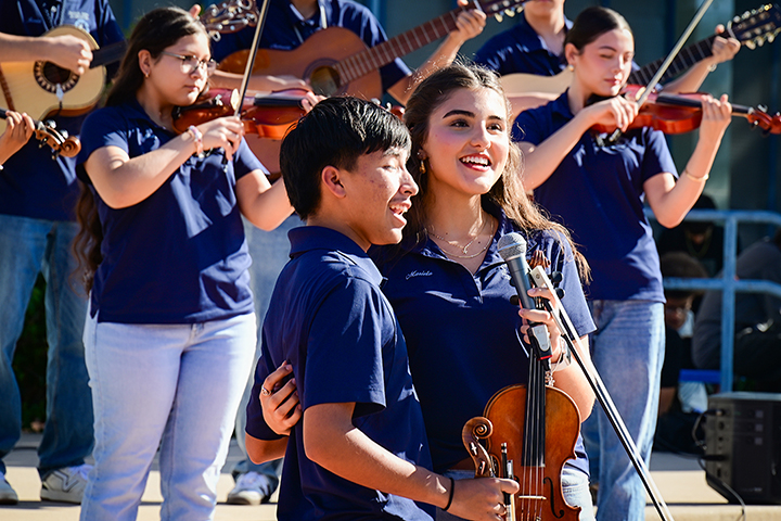 A teen boy and girl stand next to each other as they sing during a mariachi performance