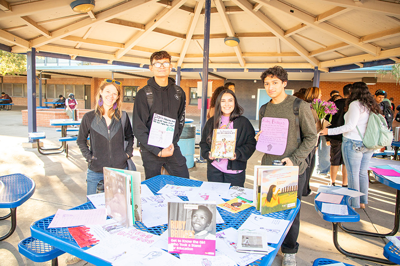 Four students stand under a gazebo holding up books about Ruby Bridges
