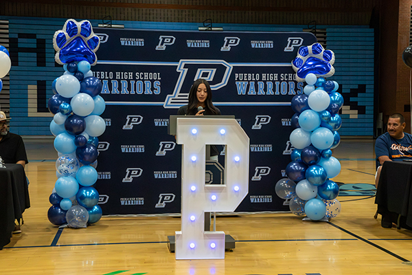 A woman stands in front of the Pueblo background and behind the Plight-up podium