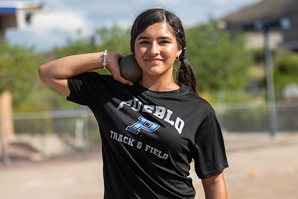 A teen girl smiles holding a shotput to her neck