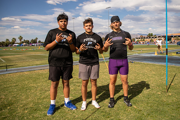 Three teen boys pose on the field