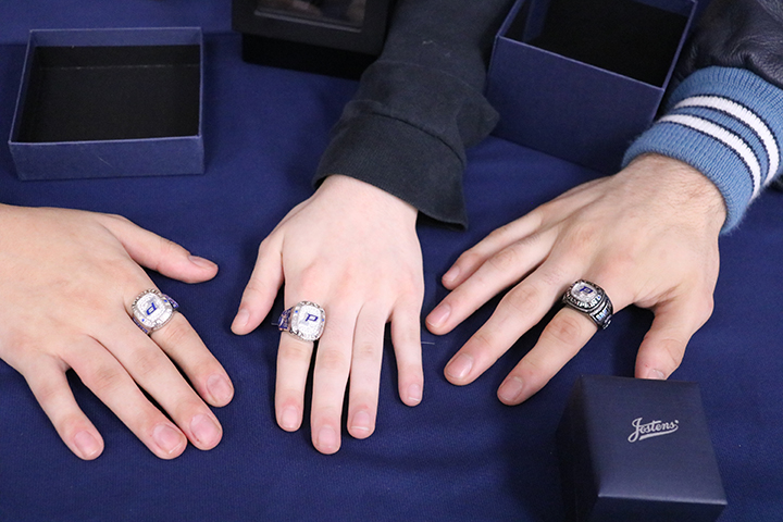 A closeup of three hands wearing a ring