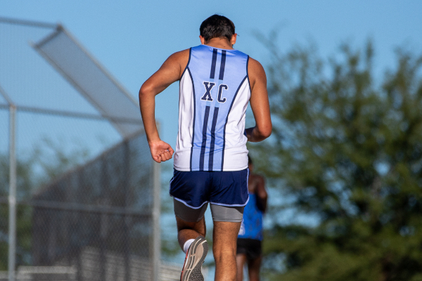 A teen boy wearing a light blue XC singlet runs on the track