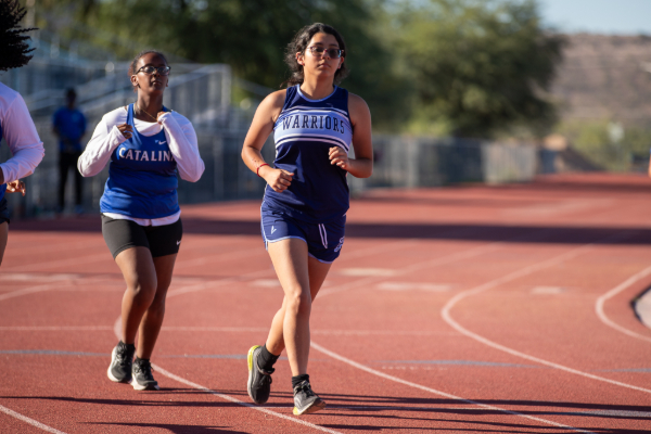 Two teen girls in blue singlets run on the track