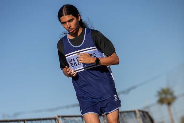 A teen boy in a blue Warriors singlet focuses hard as he runs